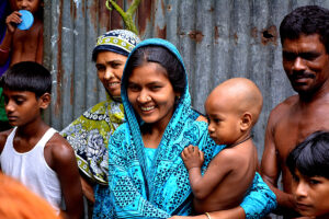 A woman holding a baby smiles with her family in a village of Bangladesh