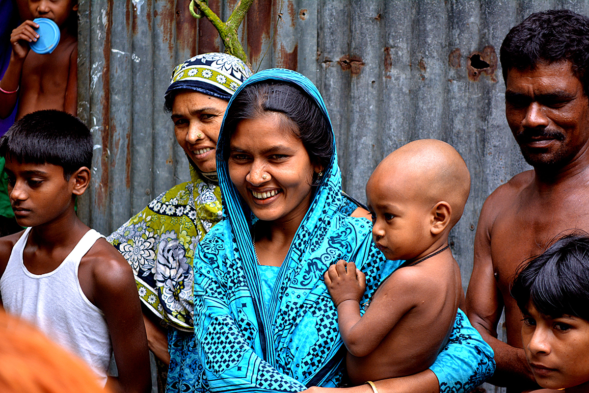 A woman holding a baby smiles with her family in a village of Bangladesh