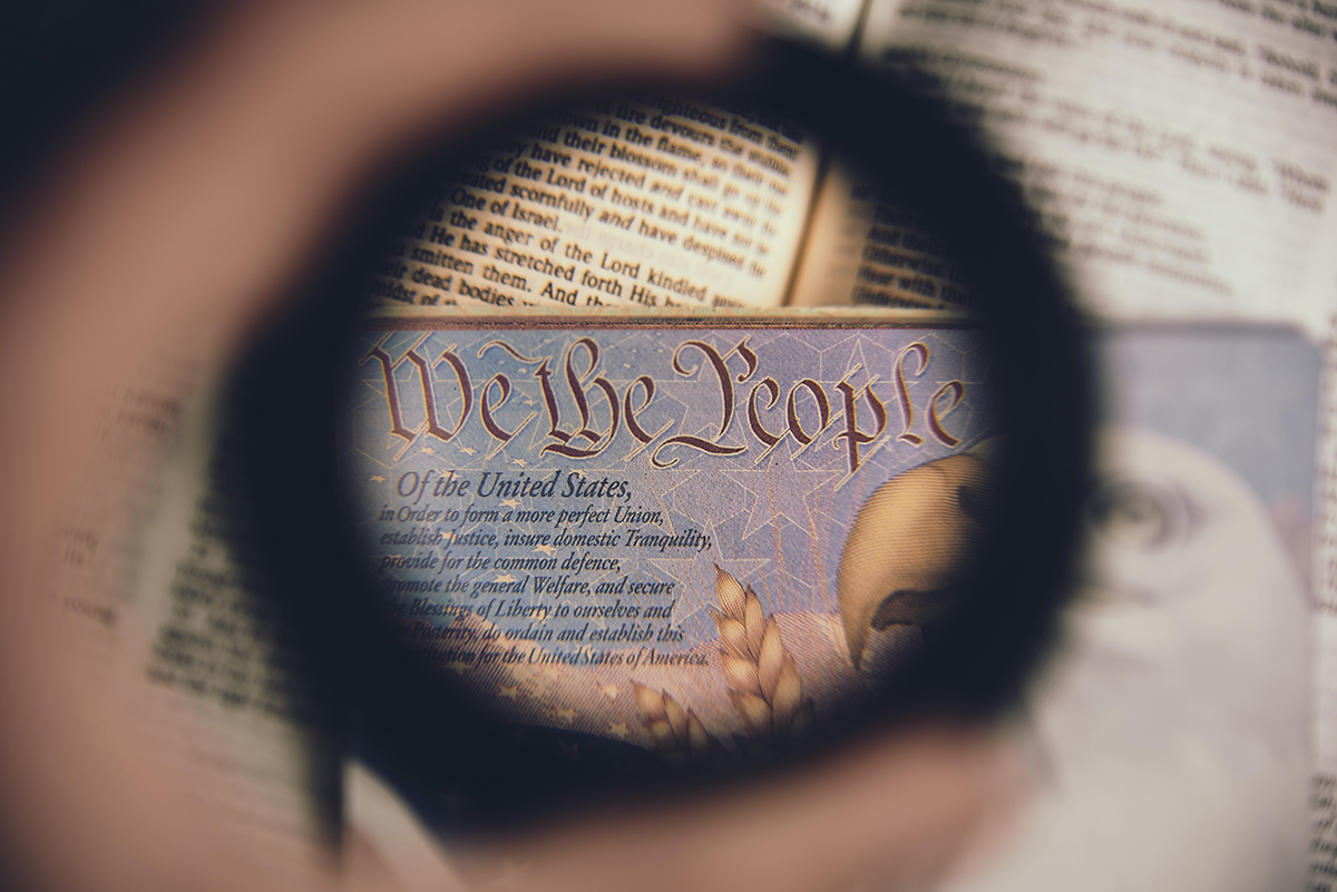 A passport page with the text of the Preamble to the United States Constitution is viewed through a magnifying glass