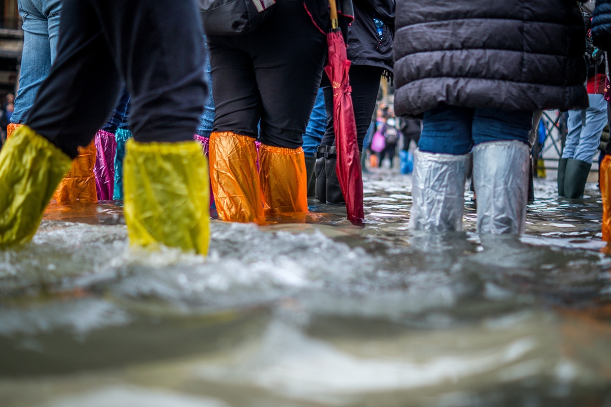 People in boots with colorful plastic bags over them walk through floodwaters