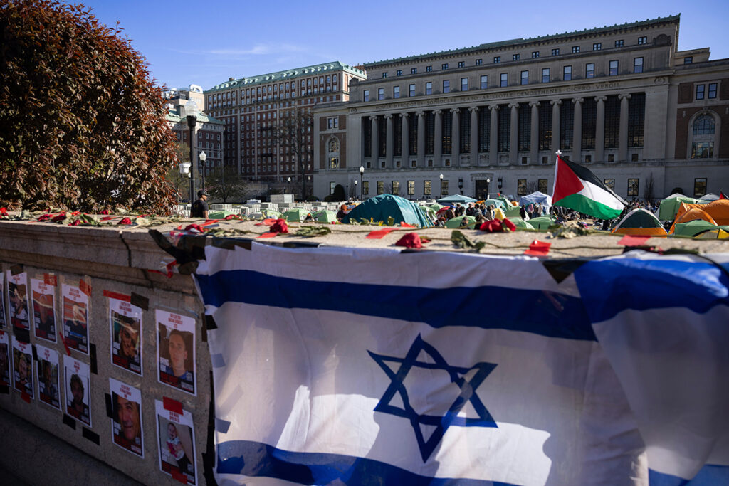In the distance, tents and Palestinian flags on the Columbia University campus in New York City. In the foreground, a makeshift memorial to Israeli hostages kidnapped by Hamas on October 7, 2023.