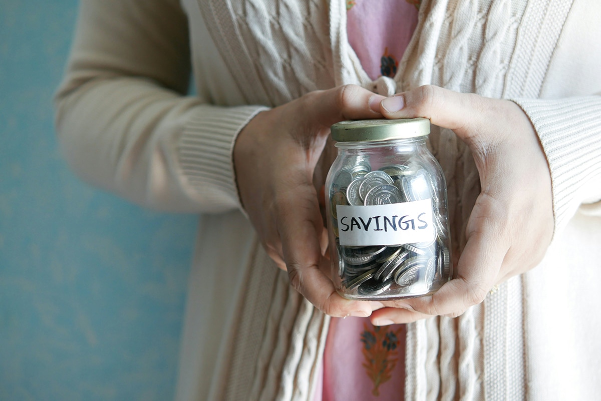 A woman holding a jar of coins labeled "savings"