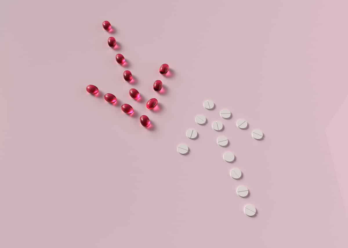 Prescription pills arranged in the shape of up and down arrows on a pink background