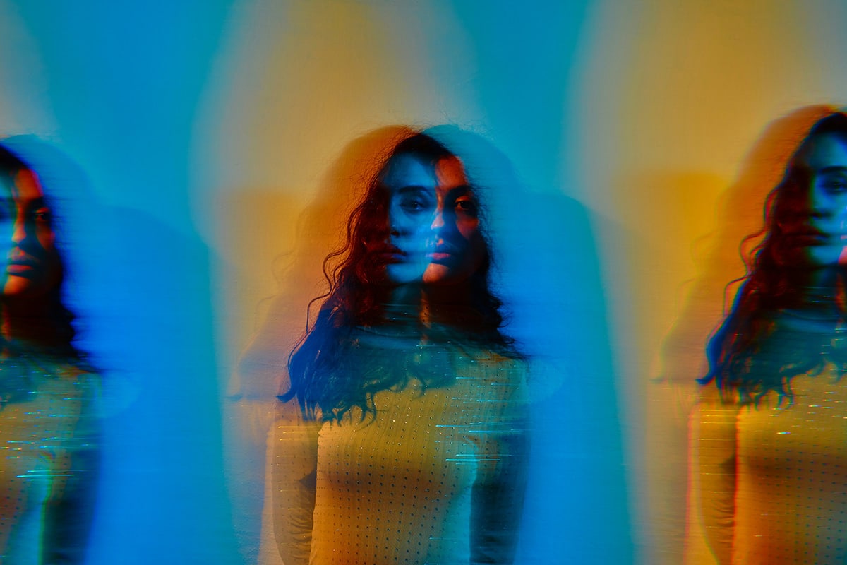 A blurred and mirrored photo of a woman in a yellow sweater standing in front of a blue wall