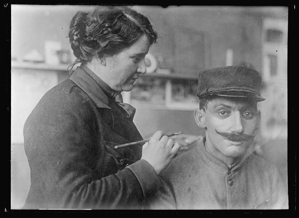 Historical photo from the early 20th century showing a woman working on a mask for men with facial mutilations