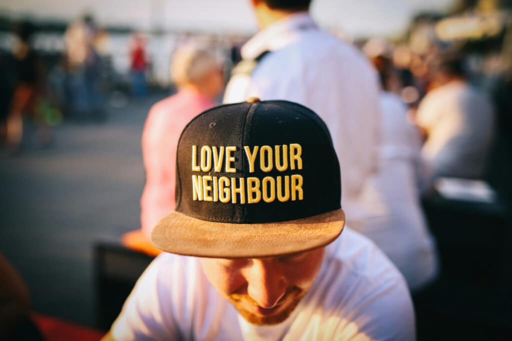 A man wearing a "Love your neighbor" hat sits outside with others in his community