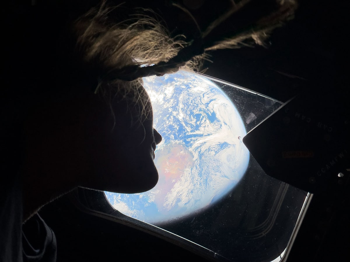 NASA astronaut and Artemis II mission specialist Christina Koch peers out of one of the Orion spacecraft's main cabin windows, looking back at Earth, as the crew travels towards the Moon. Credit: NASA